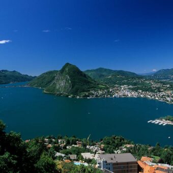 Panoramablick über den Luganer See im Tessin mit der Stadt Lugano und den umliegenden Bergen.