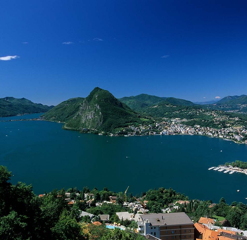 Panoramablick über den Luganer See im Tessin mit der Stadt Lugano und den umliegenden Bergen.