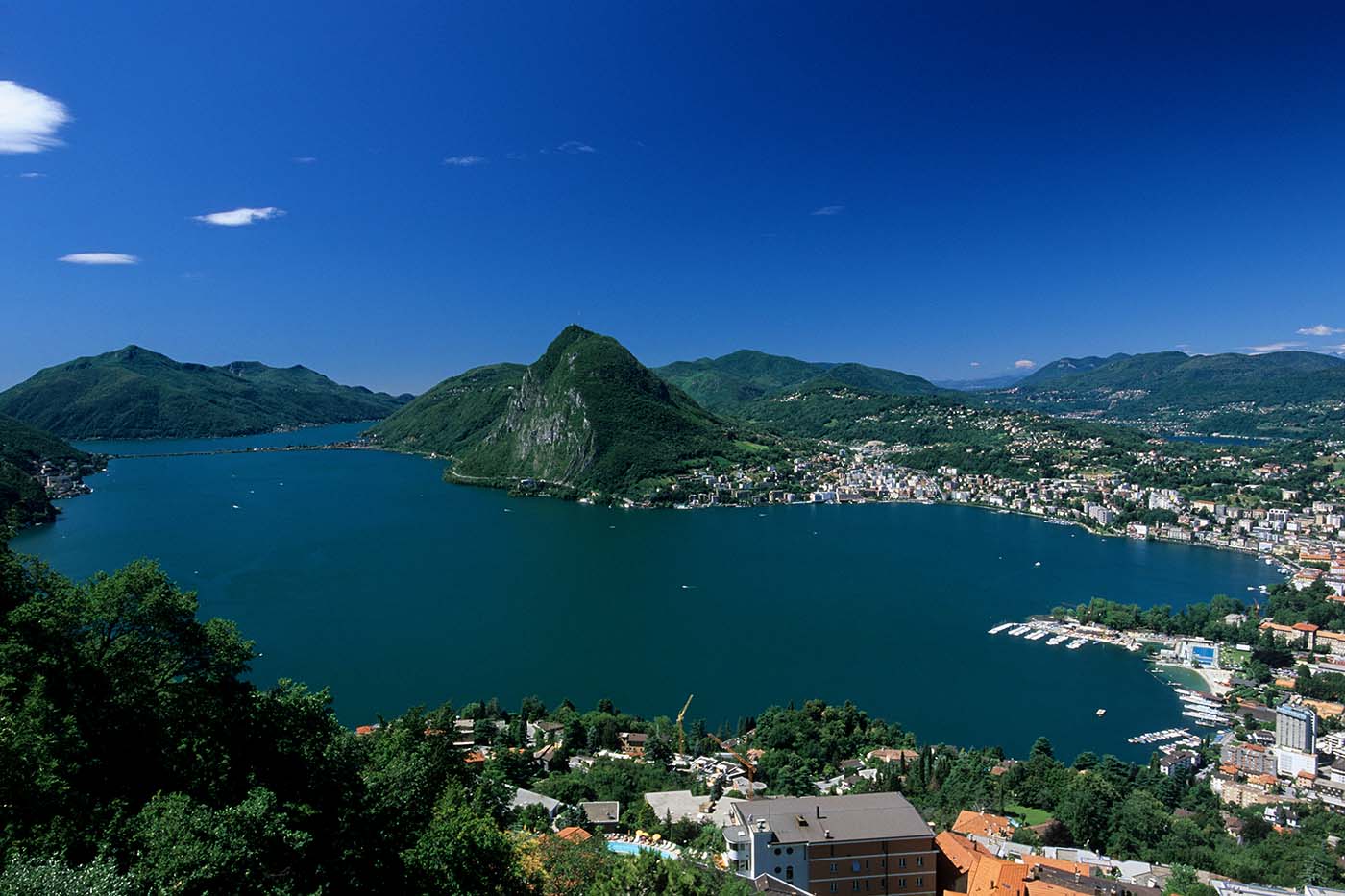 Panoramablick über den Luganer See im Tessin mit der Stadt Lugano und den umliegenden Bergen.