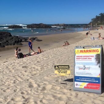 Warnschilder informieren am Strand von Sydney über die Drohnenüberwachung zur Erkennung von Haien.