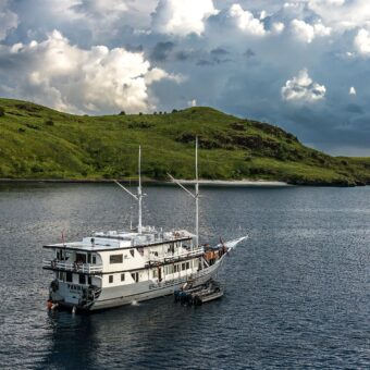 Das Tauchsafarischiff Komodo Aggressor ankert in einer Bucht zwischen grünen Hügeln im Komodo-Nationalpark