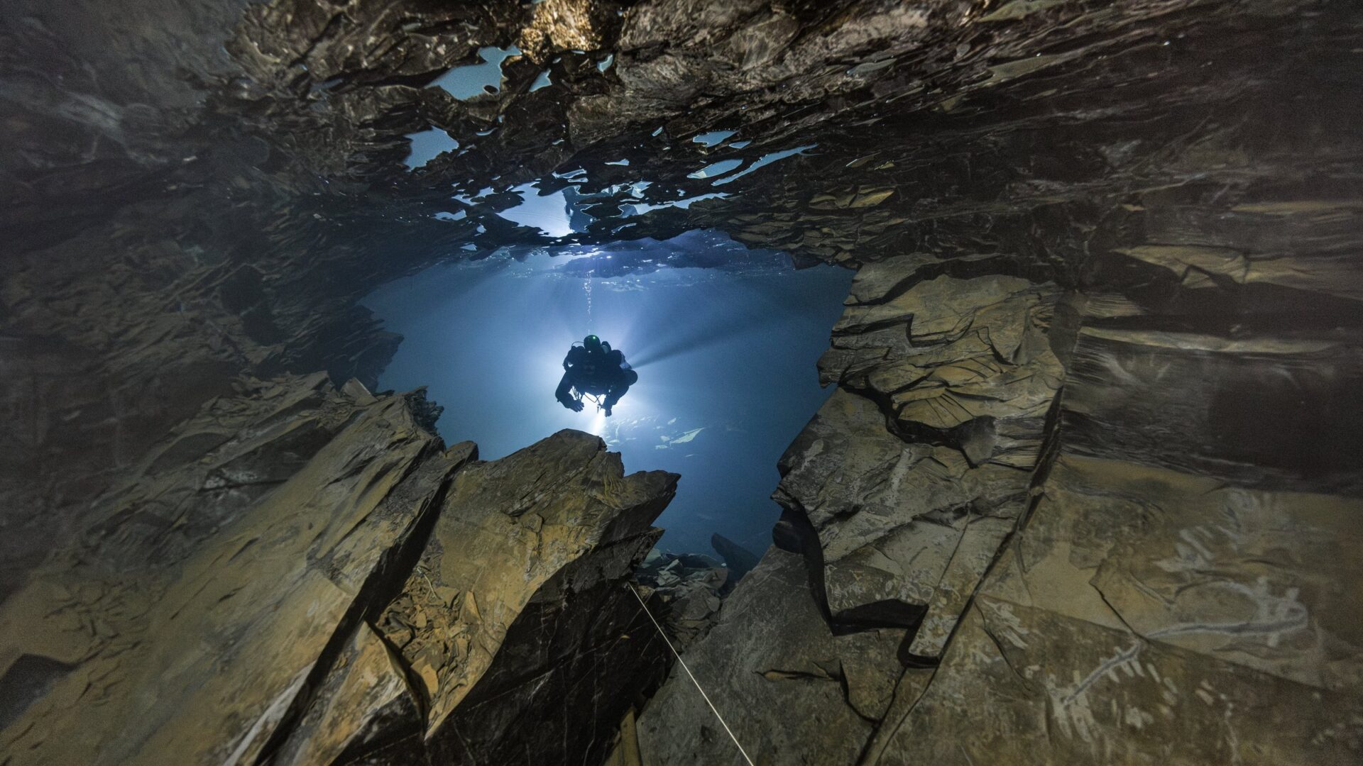 Ein Taucher schwebt im Lampenlicht durch eine Schieferhalle im gefluteten Bergwerk Nuttlar