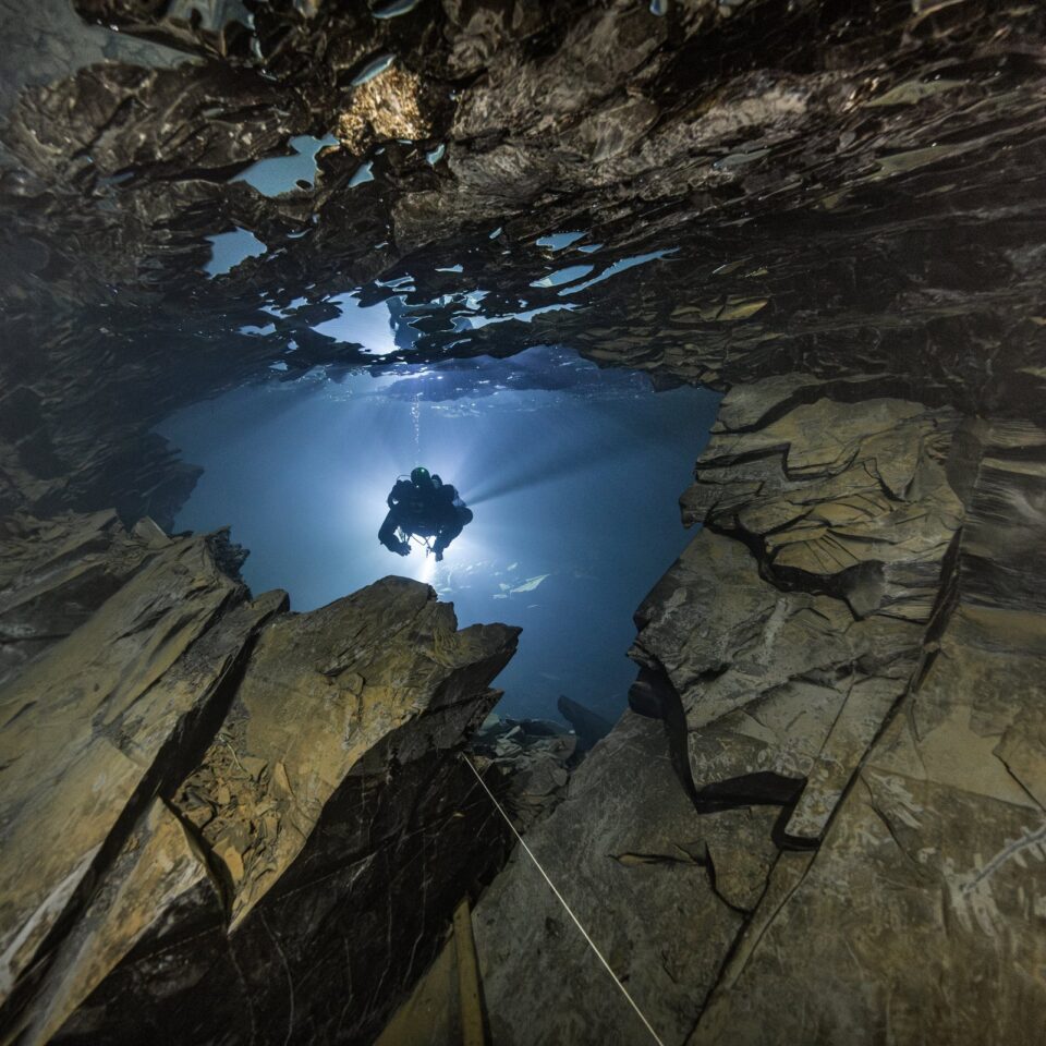 Ein Taucher schwebt im Lampenlicht durch eine Schieferhalle im gefluteten Bergwerk Nuttlar