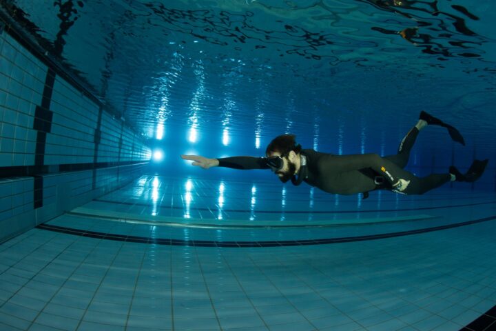 Apnoetaucher im Neoprenanzug schwimmt mit vorgestrecktem Arm auf die Beckenwand zu