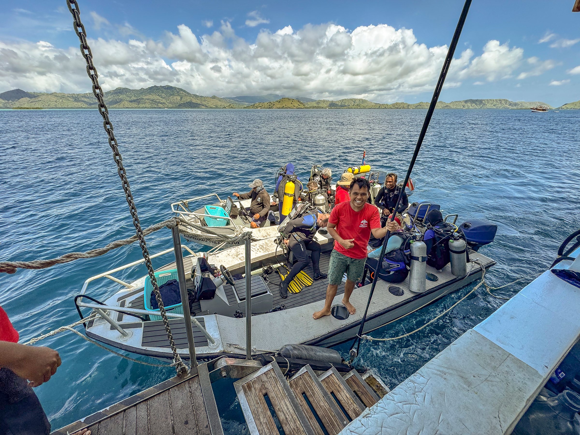 Tauchguide steht im voll besetzten Tenderboot der Komodo Aggressor, im Hintergrund die Inseln des Nationalparks