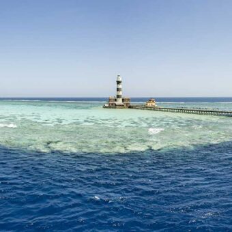 Leuchtturm auf einer Riffplattform mit langem Steg mitten im Roten Meer, im Hintergrund zwei Tauchsafarischiffe