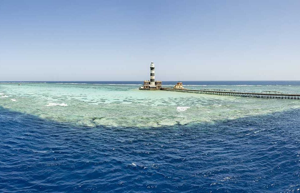 Leuchtturm auf einer Riffplattform mit langem Steg mitten im Roten Meer, im Hintergrund zwei Tauchsafarischiffe