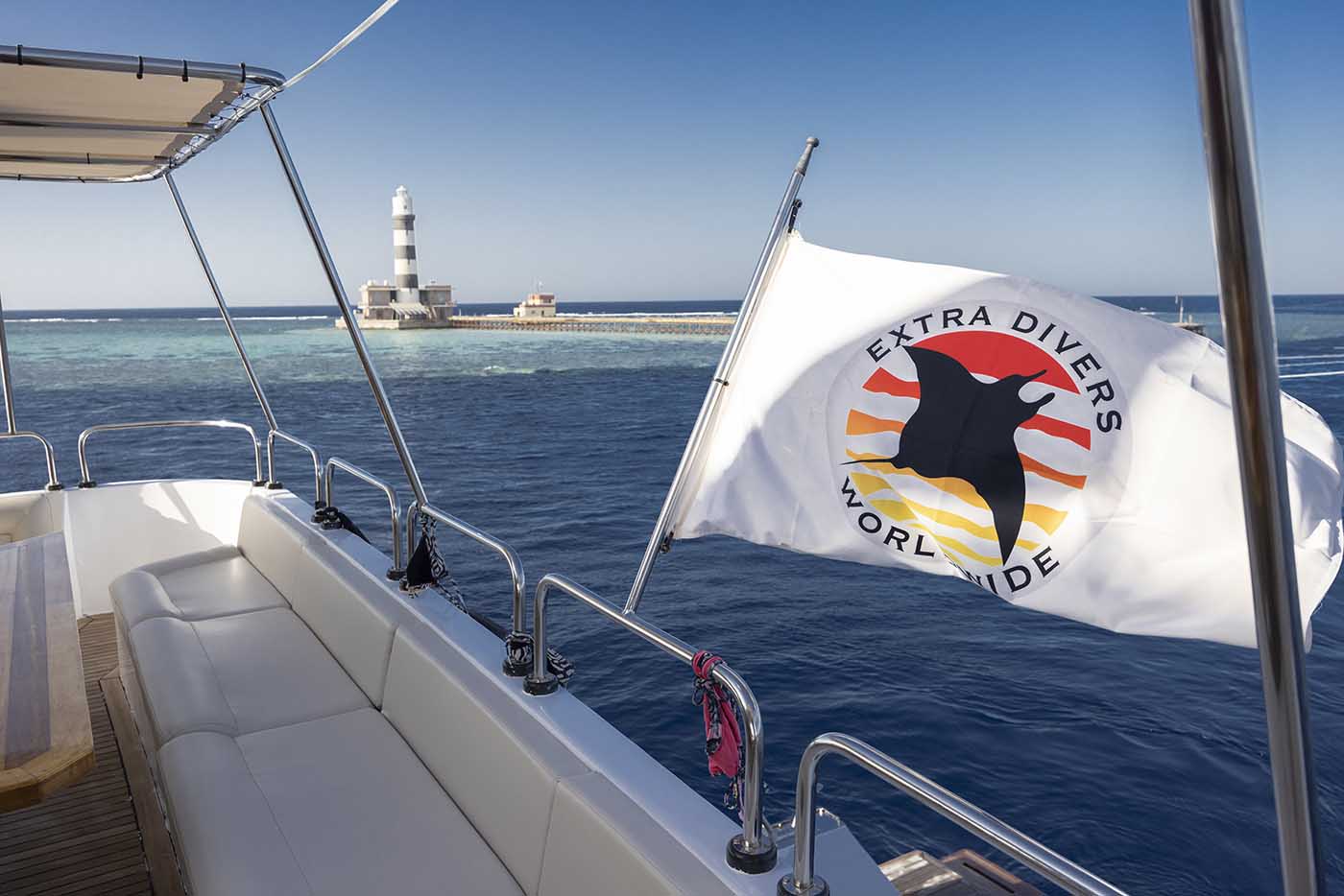 Blick vom Heck der Red Sea Explorer auf den Leuchtturm am Riff, rechts die Flagge von Extra Divers Worldwide