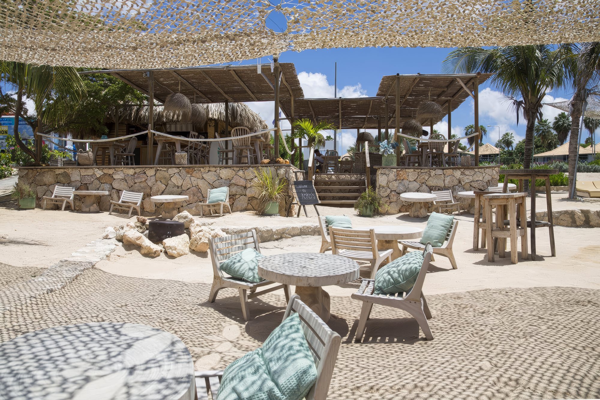 Beach-Bar mit Holzmöbeln und Schattennetzen im Sand auf Curaçao