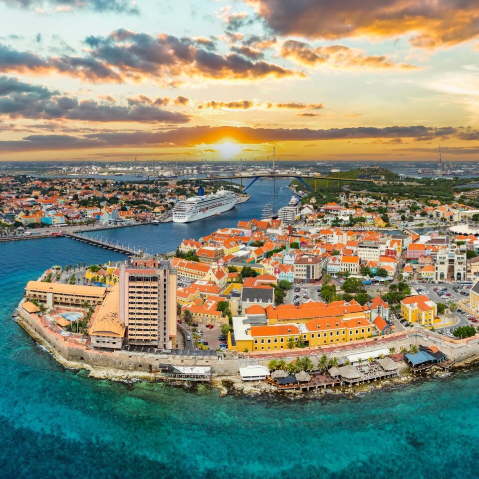 Luftaufnahme von Willemstad auf Curaçao bei Sonnenuntergang mit bunten Häusern und türkisfarbenem Meer